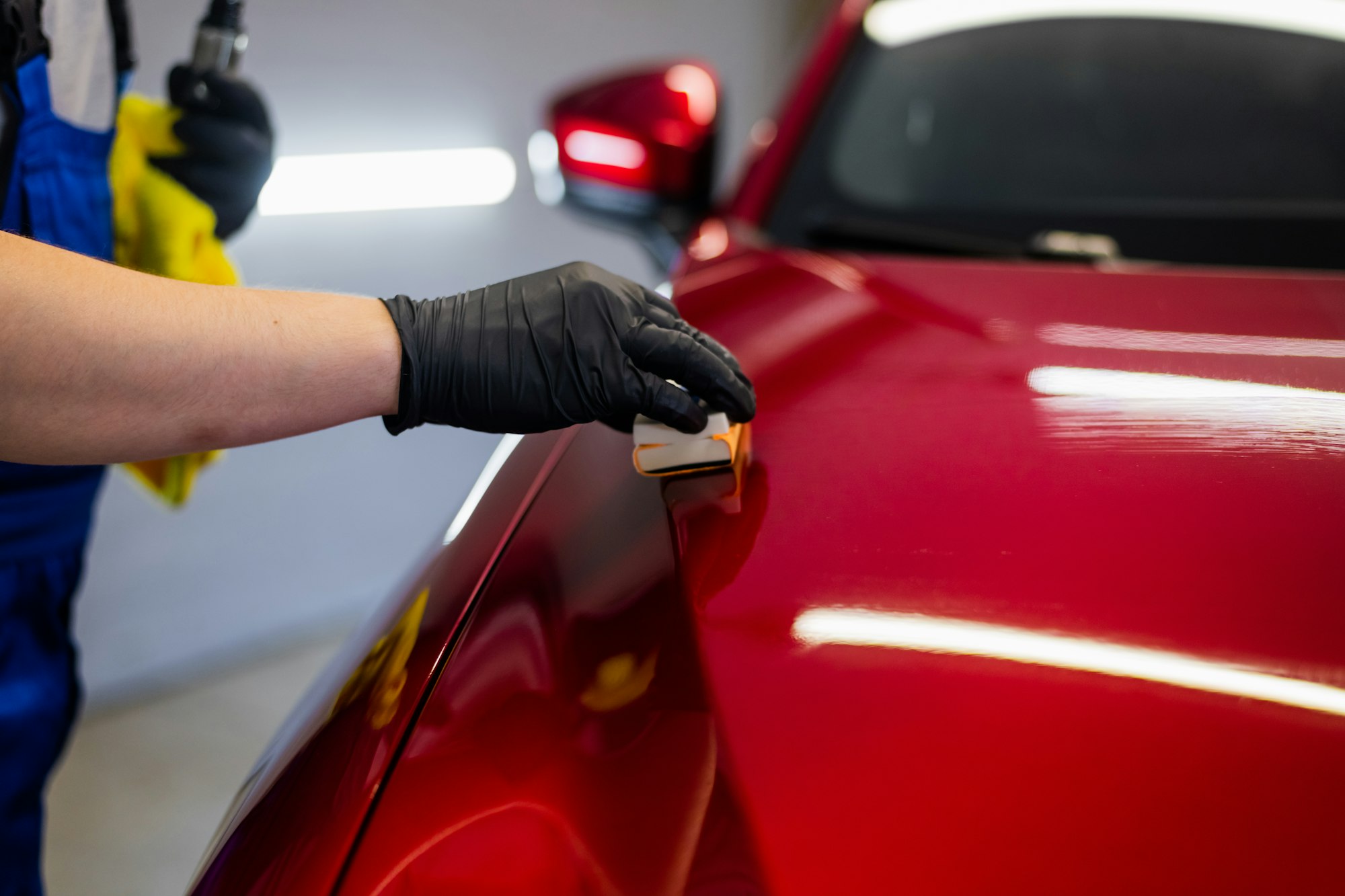 Close-up man applying ceramic coating on the red car at detailing service